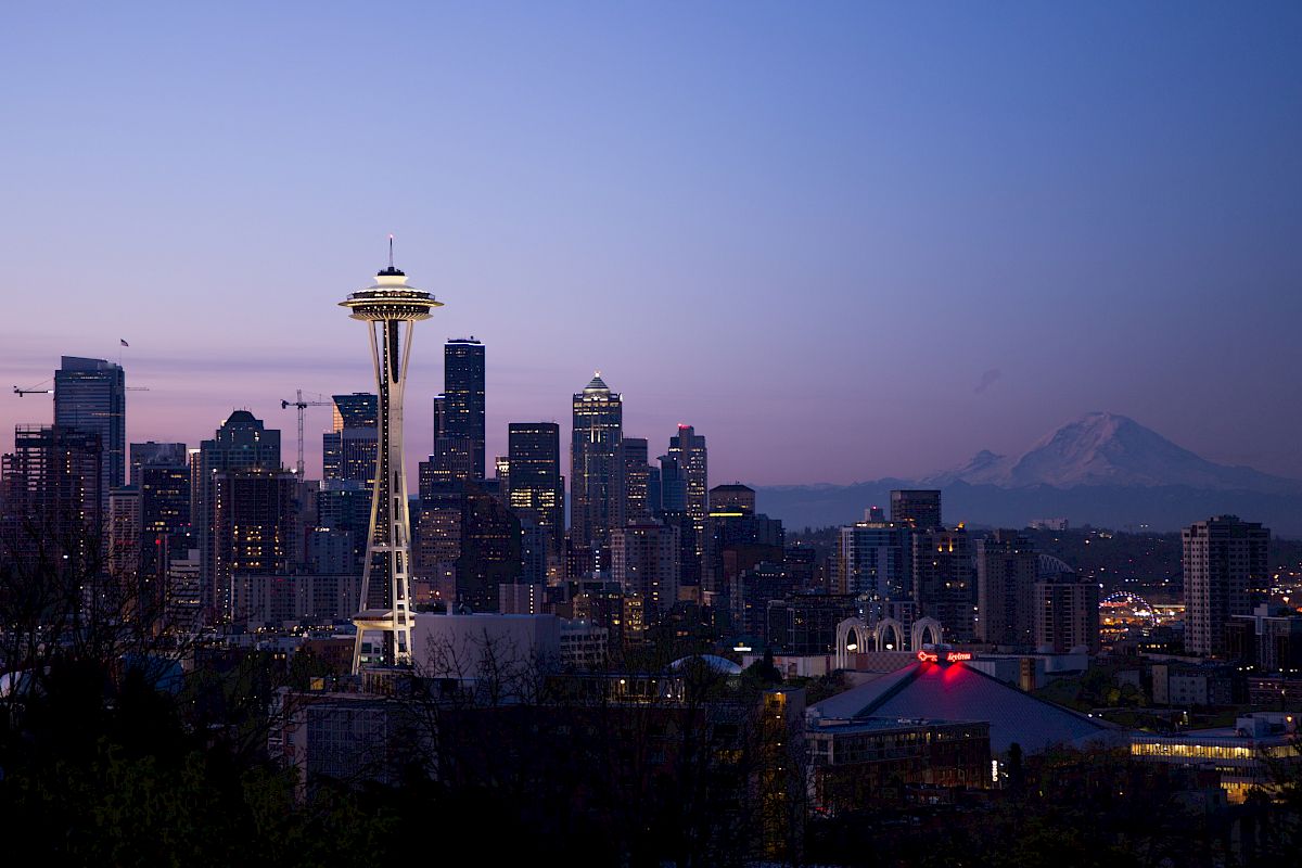 Seattle skyline at dusk with the Space Needle prominently visible and Mount Rainier in the background.