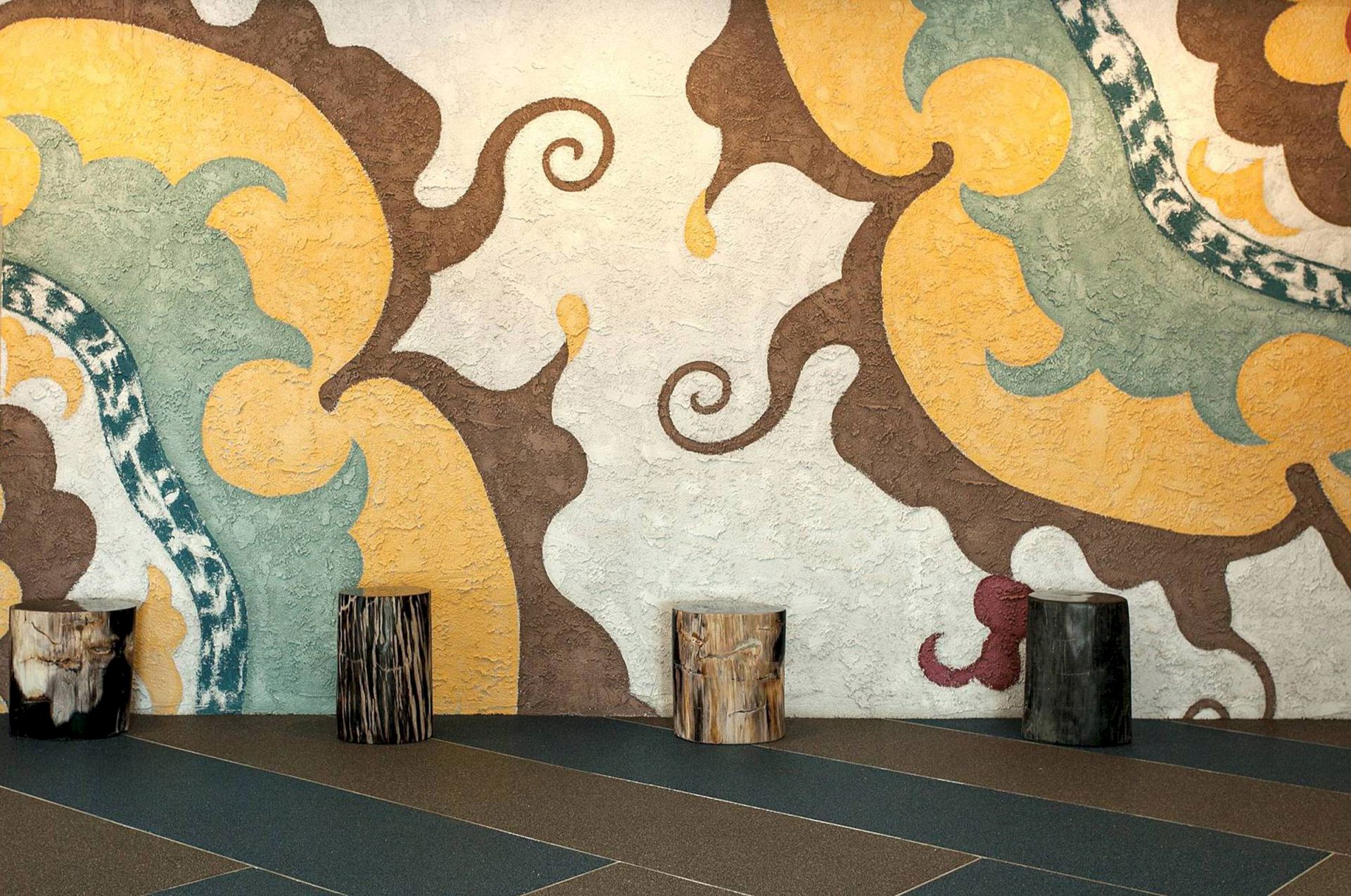 Colorful abstract wall art with swirls behind four tree stump stools on a patterned floor.
