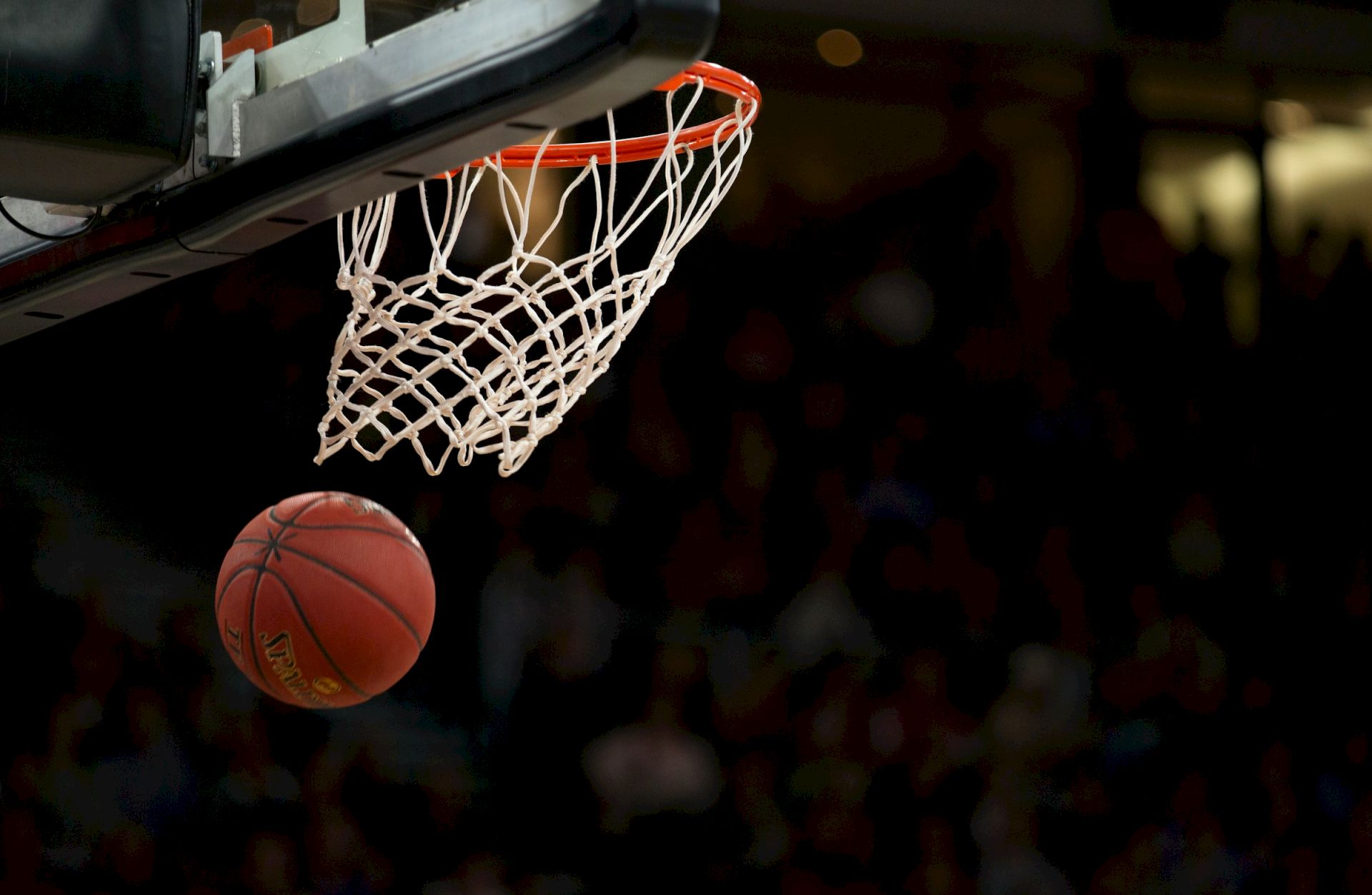 A basketball nearing the hoop, about to score, with a blurred background, likely in a gym or sports arena.