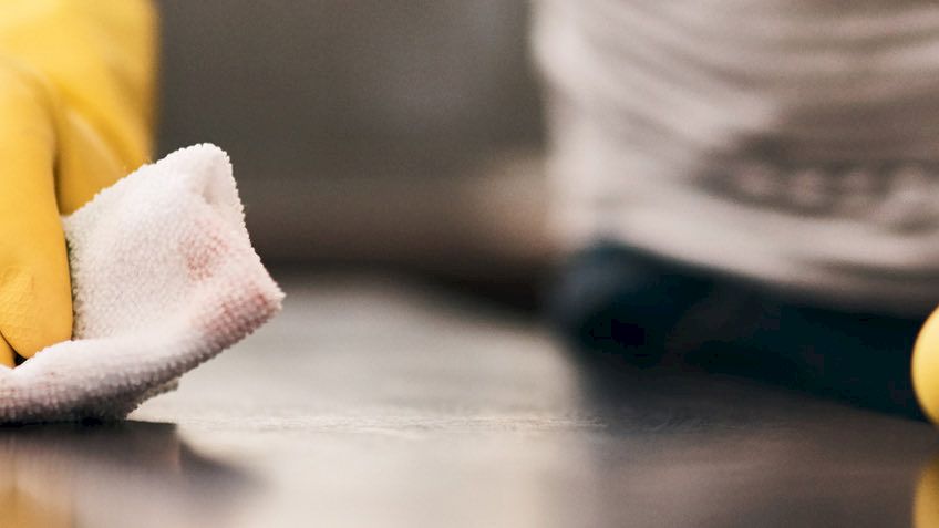 A person wearing yellow gloves cleans a surface with a white cloth.