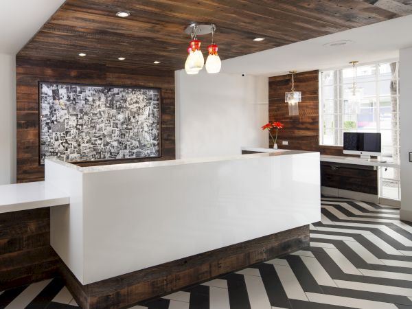 A modern reception area with a white curved desk, wood-paneled ceiling, bold black-and-white chevron floor, and a mosaic wall feature.
