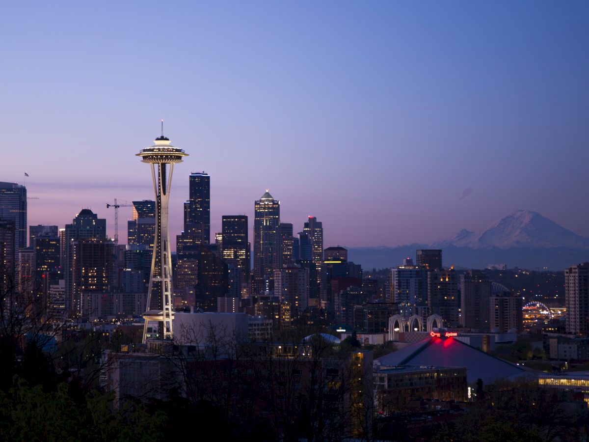 Seattle skyline at dusk with the Space Needle prominently visible and Mount Rainier in the background.