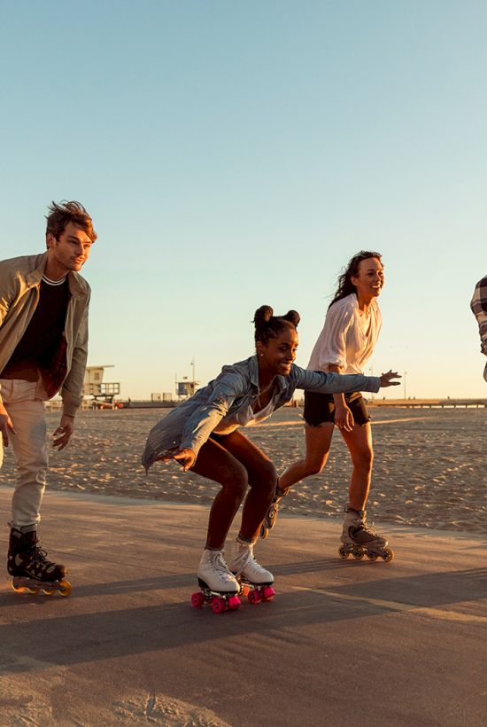 Four people rollerblading on a beachside path, enjoying sunset with palm trees in the background.