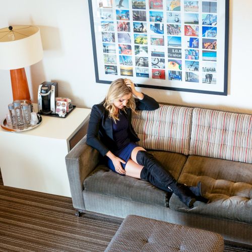 A person is sitting on a sofa beside a side table with water bottles and a coffee machine. A colorful wall collage is above.