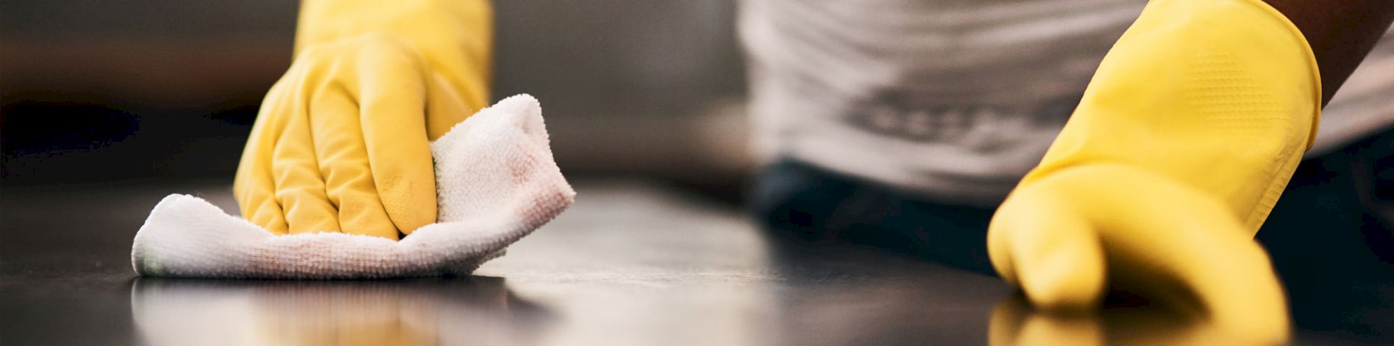 A person wearing yellow gloves cleans a surface with a white cloth.
