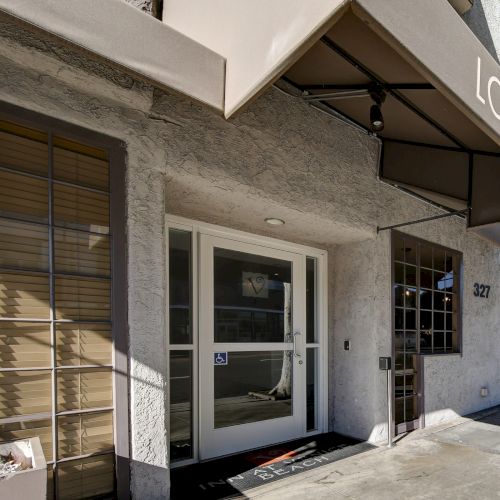 Entrance to a lobby with a glass door, awning labeled "LOBBY," window and a planter with succulents and cactus, building number 327.