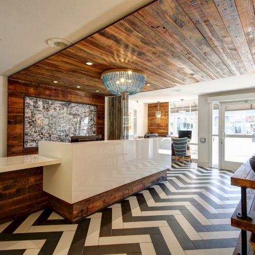 Modern lobby with wooden accents, a sleek white reception desk, geometric floor tiles, chic lighting, and potted plants.