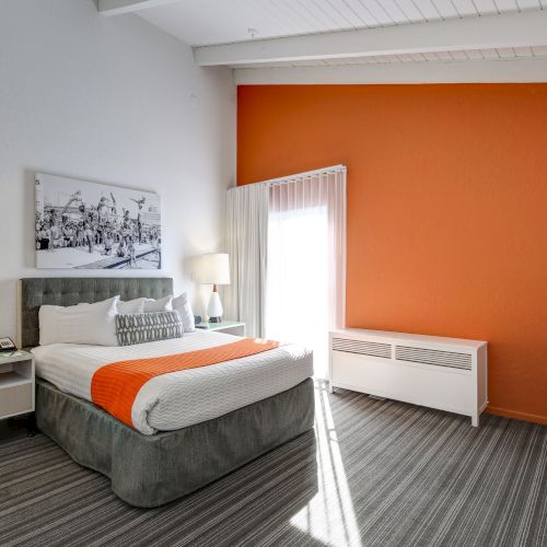 A modern hotel room with a gray bed, orange accents, two lamps, and a black-and-white wall photo. Bright and cozy atmosphere.