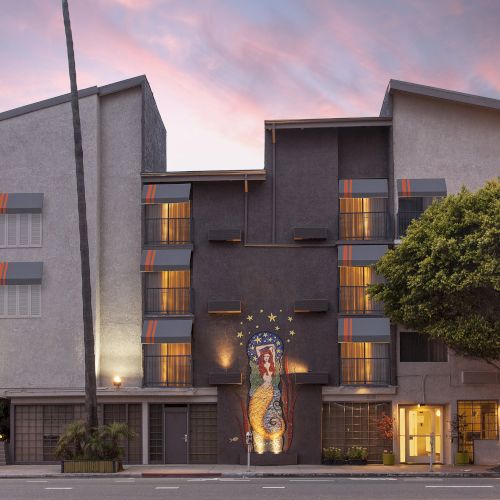A modern building with a colorful mural on the facade, surrounded by trees, under a sunset sky.