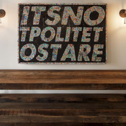 A rustic wooden table beneath a colorful sign reading "IT'S NOT POLITE TO STARE," with industrial-style wall lamps.