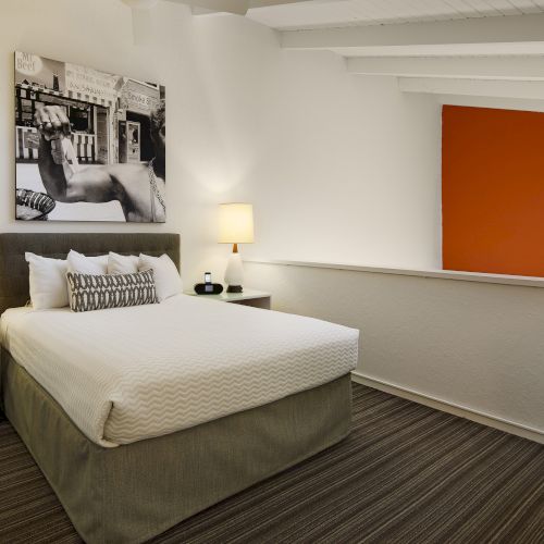 A cozy bedroom with a double bed, two lamps, a black-and-white wall picture, and an orange accent wall.