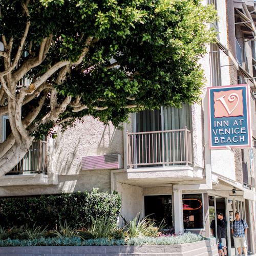 A hotel named "Inn at Venice Beach" with a large tree in front. Two people walk nearby, and there's a sign for Sanborn Ave.
